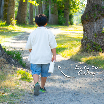 Bouteille Santevia Kids Ivory tenue par un enfant marchant sur un sentier de parc forestier. Facile à transporter