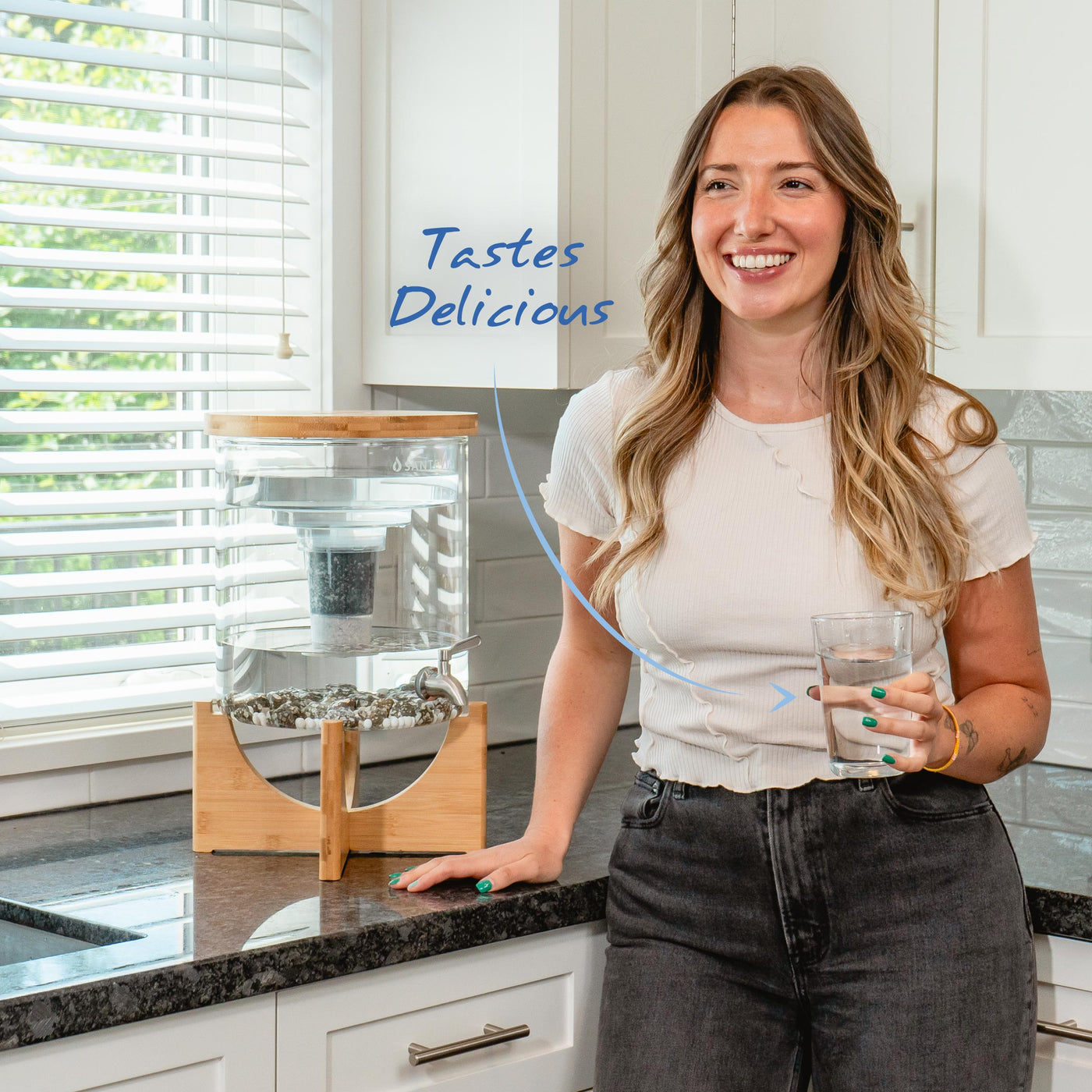 Women smiling in a kitchen drinking a glass of mineral water from the Santevia Glass Water System