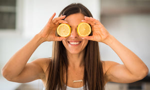 Woman smiling while holding a round slice of lemon over each eye